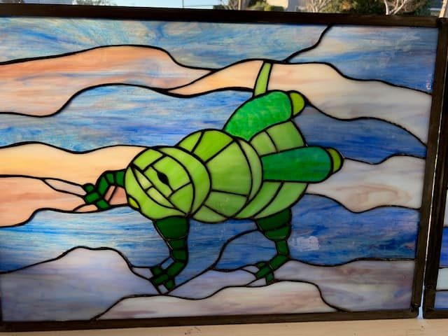 Student stained glass sea turtle in bright green over a soft watercolor sky