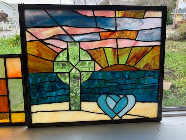 Stained glass sunrise panel with cross and interlocking hearts in orange, teal, and gold
