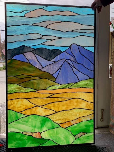 Large stained glass mountain landscape panel in blues, greens, and gold