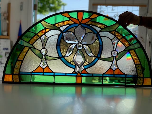 Arched stained glass transom with beveled floral medallion in green and orange