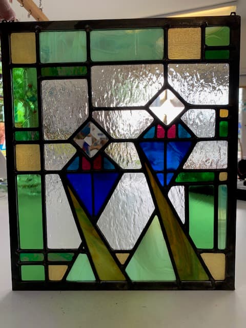 Geometric stained glass panel with stylized mountain peaks in blue, green, and gold