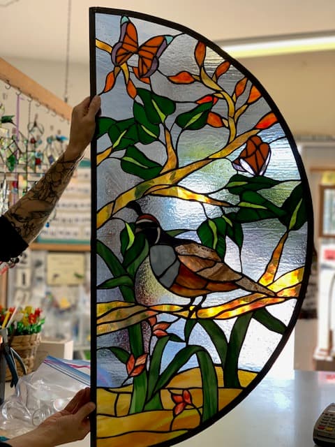 Half-circle stained glass panel with quail on a branch and butterfly among foliage