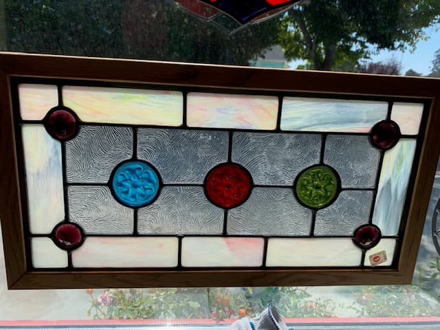 Victorian-style stained glass panel with decorative colored roundels in wood frame